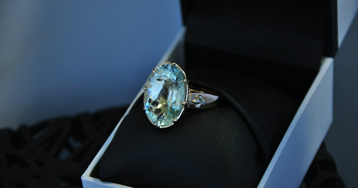 A silver ring with a blue topaz resting in a gift box, showing the gem's faceted sparkle